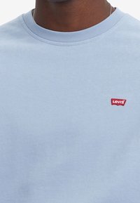 Camiseta de algodón azul claro con cuello redondo y un pequeño logo rojo de Levi's cosido en el área izquierda del pecho. Textura suave, corte casual.