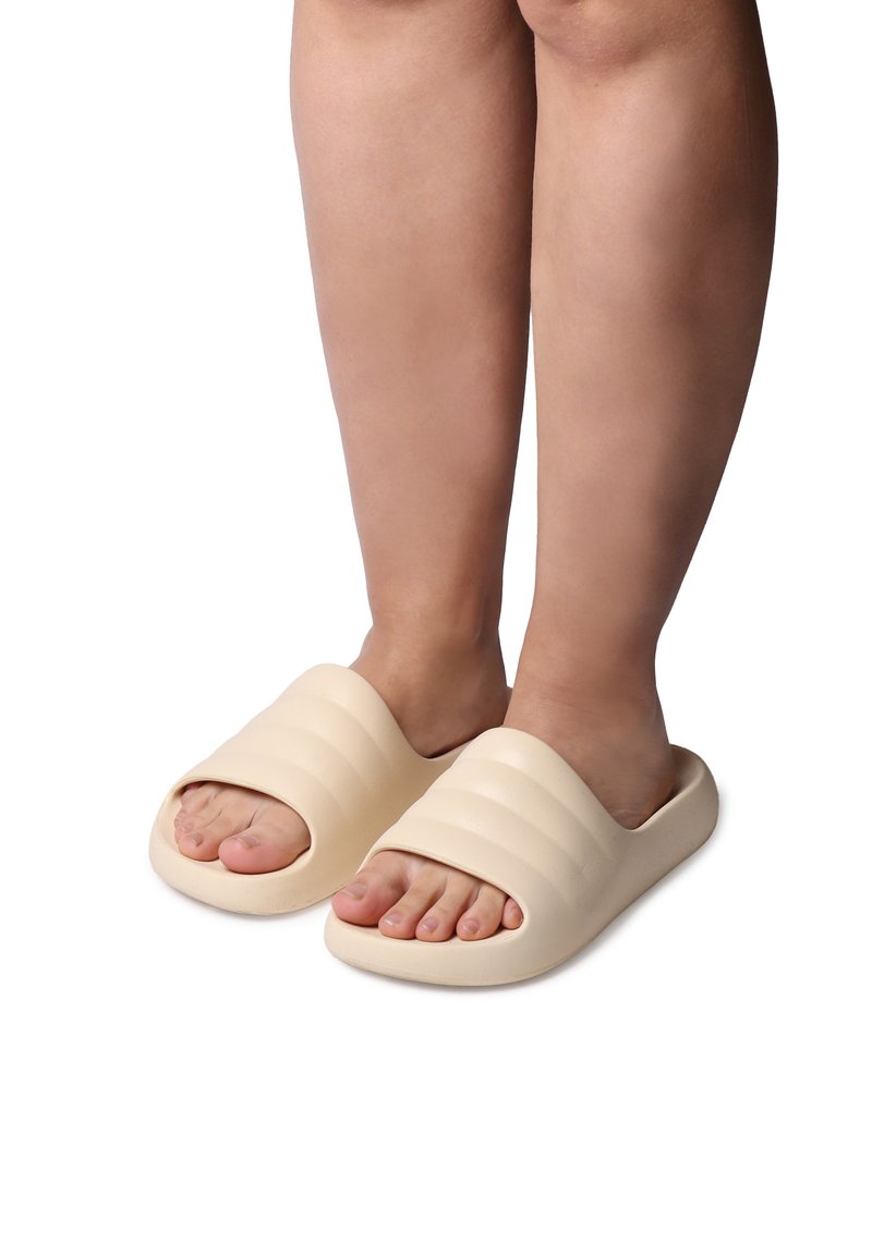 Infradito beige con una fascia larga e ondulata, design con punta aperta e una suola liscia e arrotondata. Adatte per uso interno o esterno.