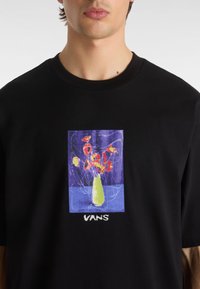 Schwarzes Baumwoll-T-Shirt mit einem bunten Grafikdesign eines Vasen mit Blumen auf blauem Hintergrund. "VANS"-Logo am unteren Ende. Rundhalsausschnitt.