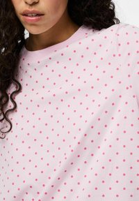 Vaaleanpunainen T-paita pyöreällä kaula-aukolla, jossa on toistuva kuvio pienistä kirkkaanpunaisista pilkuista. Pehmeää puuvillakangasta, jossa on sileä rakenne.