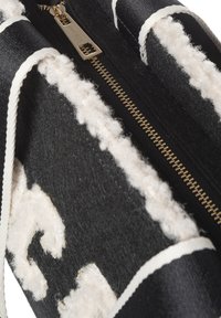 Zwarte tas met ritssluiting en een gestructureerd wit wollen accent. Voorzien van een gouden ritssluiting en een zwart-wit gestreepte stoffen detail.