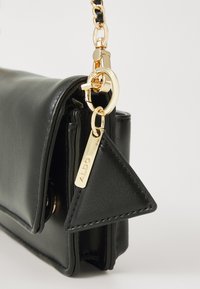 Black leather handbag with a folded design, featuring a gold chain strap and triangular tag. Smooth texture and gold hardware accents.