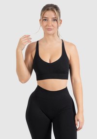 Sujetador deportivo negro con una banda ancha, escote en V profundo y tirantes delgados, combinado con leggings negros de cintura alta. Tejido liso y elástico.