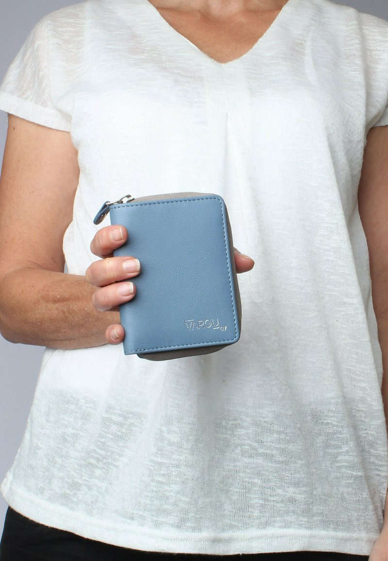 Blue leather wallet with a zip closure, rectangular shape, smooth texture, and light gray accents. Displayed in a hand against a white shirt.