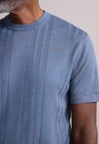 Pull tricoté bleu clair à manches courtes avec des motifs de points verticaux et un col rond côtelé. Texture lisse et coupe ajustée.