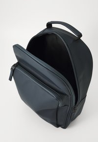 Námornícky modrý batoh vyrobený z hladkého materiálu; má vrchnú rúčku, hlavný oddelený priestor so zipsom a predné vrecko s elegantným dizajnom.
