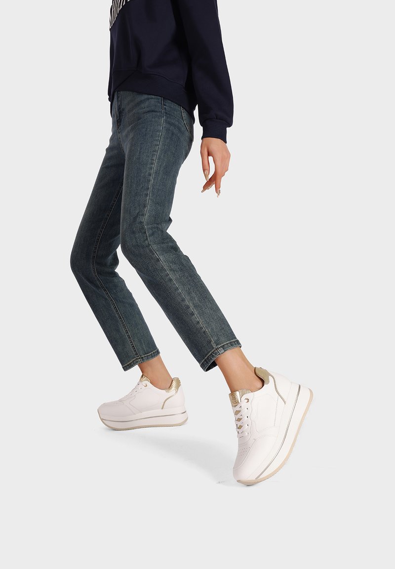 Sneaker bianche con accenti dorati, upper in pelle liscia, suola imbottita e silhouette stretta. Indossate con jeans di denim blu.