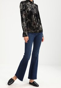 Black floral-printed velvet top with a zip neck, paired with flared dark blue denim jeans and black slip-on shoes.