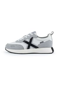 Zapatilla gris y blanca con parte superior de ante y lona texturizada, que presenta un diseño de cruz negro, cierre de cordones y suela de goma blanca.