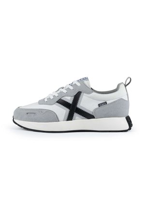 Zapatilla gris y blanca con parte superior de ante y lona texturizada, que presenta un diseño de cruz negro, cierre de cordones y suela de goma blanca.