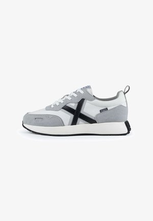 Zapatilla gris y blanca con parte superior de ante y lona texturizada, que presenta un diseño de cruz negro, cierre de cordones y suela de goma blanca.