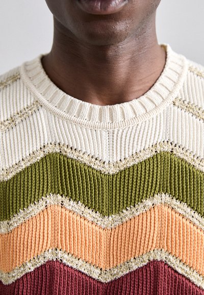 Adīts džemperis ar zigzaga svītrām krēmkrāsā, olīvu zaļā, persiku un bordo krāsā. Strukturēta dzija ar ribotu kakla izgriezumu un vieglu spīdumu.