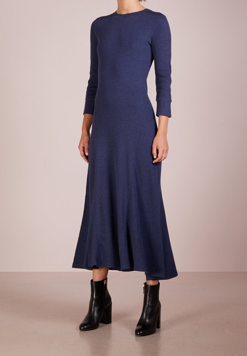 Robes longues de couleur marine à manches longues avec un corsage ajusté, une jupe évasée, une texture côtelée et des coutures accentuées. Porté avec des bottines à talons carrés noires.