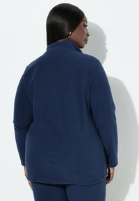 Granatowy polarowy pulower z wysokim kołnierzem i długimi rękawami. Gładka faktura, długość do talii oraz luźny krój, odpowiedni do warstwowego ubioru.