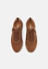 Bruna mockasnörskor med en texturerad detalj nära snörningen, rund tå och en sidodragkedja. Har bruna snören och en ljusfärgad sula.