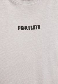 Jasnoszary materiał z czarnym tekstem w stylu szablonowym "PINK FLOYD" nadrukowanym blisko górnego środka.