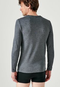Grijs shirt met lange mouwen en een ronde hals, gemaakt van zachte stof. Het heeft een eenvoudig ontwerp en een getailleerde snit zonder zichtbare patronen of accenten.