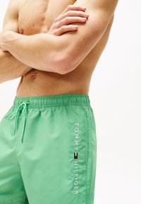 Bañador verde con cintura elástica y cordón. Presenta un logo y texto en blanco en el costado, fabricado con un tejido suave y ligero.