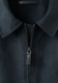 Col col et fermeture partiellement zippée à l'avant d'une veste bleu marine foncé avec une fermeture éclair métallique visible et un curseur en cuir.