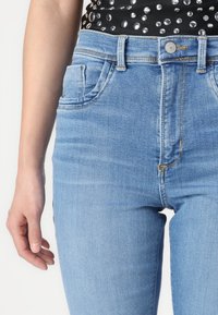 Jeans de tiro alto azul claro con un diseño clásico de cinco bolsillos, textura desgastada y costuras visibles a lo largo de las costuras.