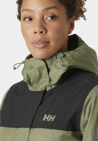 Chaqueta resistente al agua en verde y negro, con un alto cuello, cordones ajustables y un logo en el pecho. Textura suave.