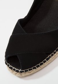 Espadrille noire avec un design à bout ouvert, tige en tissu doux et semelle enveloppée de jute avec des coutures le long du bord.