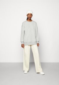 Gray sweatshirt with round neck and dropped shoulders, paired with cream wide-leg trousers and white sneakers. Model wears a white beanie.
