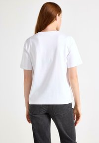 Hvid bomulds T-shirt med korte ærmer, en klassisk rundhalsudskæring og en afslappet pasform, parret med mørkegrå jeans. Glat tekstur.