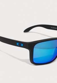 Schwarze Sonnenbrille mit blauen verspiegelten Gläsern, rechteckiger Form, mattes Finish, mit einem blauen Akzent am Bügel und zwei kleinen Schrauben.