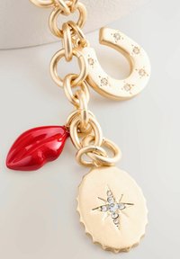 Zlatý náhrdelník s obručkovými článkami, charm v tvare podkovy s kryštáľmi, červený lesklý tvar pier a oválny prívesok so vzorom hviezdy a kamienkami.