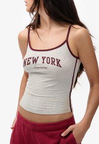 Graues Tanktop mit weinrotem Besatz, das den Schriftzug "NEW YORK" zeigt und eine figurbetonte Passform hat. Weicher Stoff, Spaghettiträger und schlanke Silhouette.