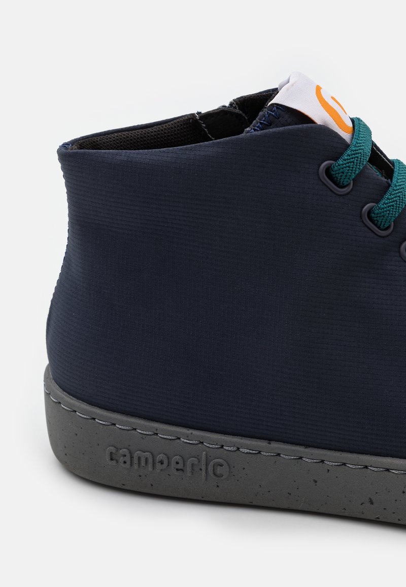 Marine højtop sko med tekstureret stof, grønne snørebånd og en spraglet grå sål. Har et logo-patch på den øverste kant.