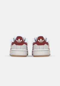 Zapatillas blancas de cuero con acentos rojos, superposiciones texturizadas y suela de goma. Presentan un logo de tres franjas y un cuello acolchado.