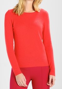 Rode sweater met lange mouwen, ronde halslijn, ribbelrand en ribgebreide boorden. Zachte textuur, ongecompliceerd ontwerp, gecombineerd met roze broeken.