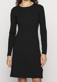 Robe noire à manches longues en tissu lisse et extensible, avec un col rond et un ourlet légèrement évasé. Design minimaliste, sans motifs visibles.