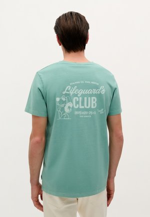 Mintgroene katoenen t-shirt met een ronde hals; de achterkant heeft een grafische print van een hond en de tekst "Lifeguard's CLUB" in het wit.