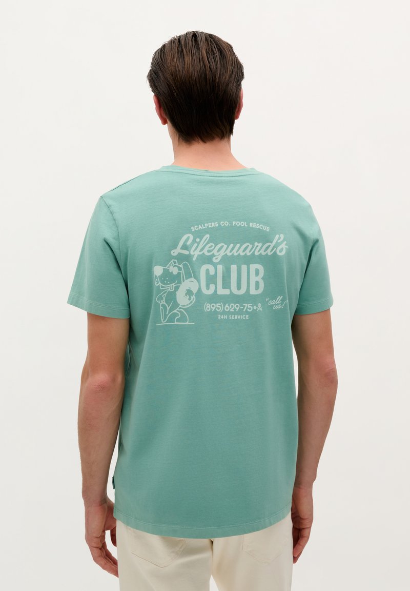 Mintgroene katoenen t-shirt met een ronde hals; de achterkant heeft een grafische print van een hond en de tekst "Lifeguard's CLUB" in het wit.