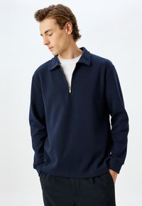 Navyblauwe zip-up trui met een gestructureerd ribpatroon, voorzien van een klassieke kraag en een kwartlange rits voor eenvoudig aan- en uittrekken.
