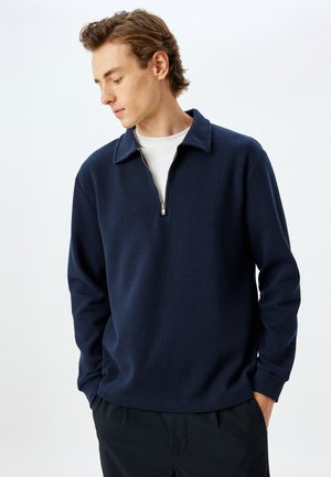 Sudadera azul marino con cremallera, con un diseño de canalé texturizado, que presenta un cuello clásico y una cremallera de un cuarto de longitud para facilitar su uso.