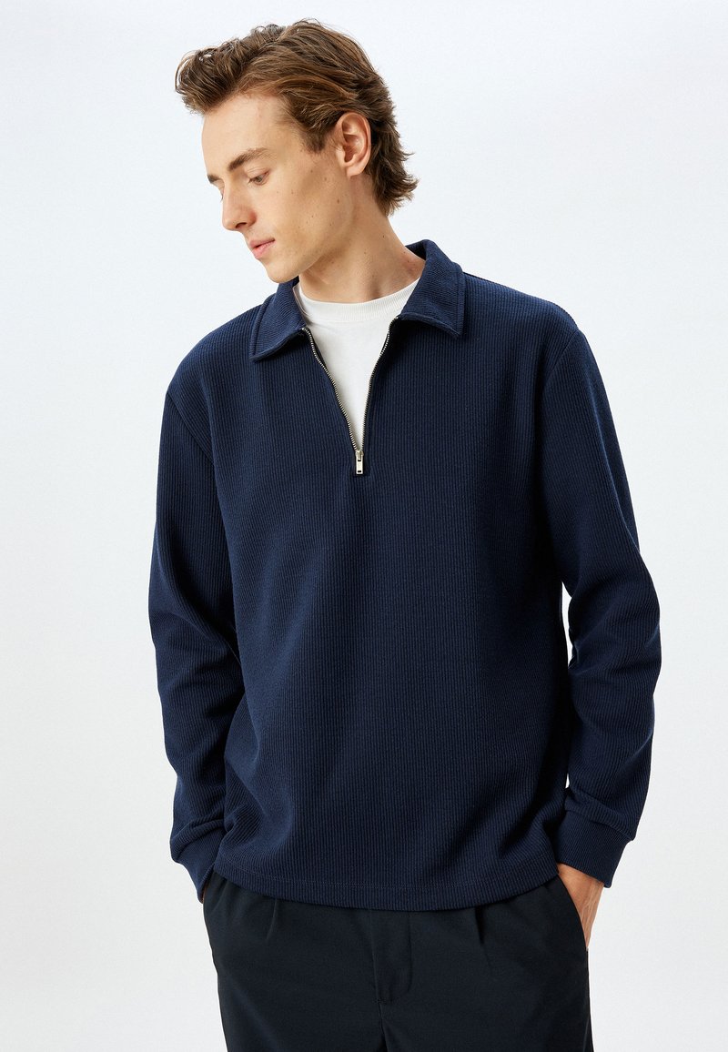 Navyblauwe zip-up trui met een gestructureerd ribpatroon, voorzien van een klassieke kraag en een kwartlange rits voor eenvoudig aan- en uittrekken.