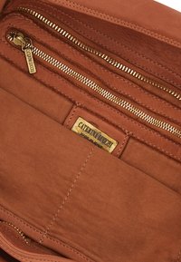Interno in tessuto marrone di una borsa, con una tasca con zip e un'etichetta brandizzata. Texture liscia con accessori in oro e cuciture a contrasto.