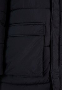 Crna puffer jakna s matt površinom, koja ima džep na prsima, kviltani uzorak i elastičnu donju ivicu. Mekana tekstura i lagani dizajn.