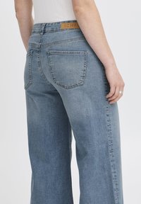 Jeans in denim di un azzurro chiaro a vita alta, con un taglio dritto e ampio, dotati di due tasche posteriori e una patch in pelle con il marchio in vita.