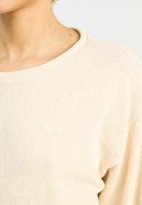 Beige gebreide trui met een ronde halslijn. Kenmerkt zich door een subtiele hartlogo, textuurstof en een ontspannen pasvorm.