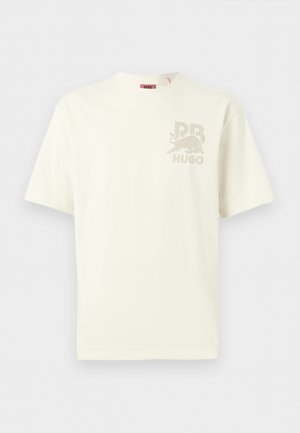 T-shirt à manches courtes de couleur écrue avec un petit motif beige représentant un taureau, les lettres doubles "RR", et le texte "HUGO" sur le côté gauche de la poitrine.