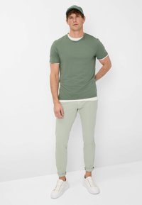 T-shirt verde a maniche corte con bordi bianchi, abbinato a pantaloni verde chiaro e scarpe da ginnastica bianche. Il cappellino è dello stesso colore della maglietta.