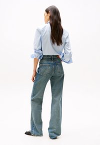 Light blue long-sleeve shirt with rolled cuffs paired with high-waisted light blue straight-leg jeans featuring patch back pockets.