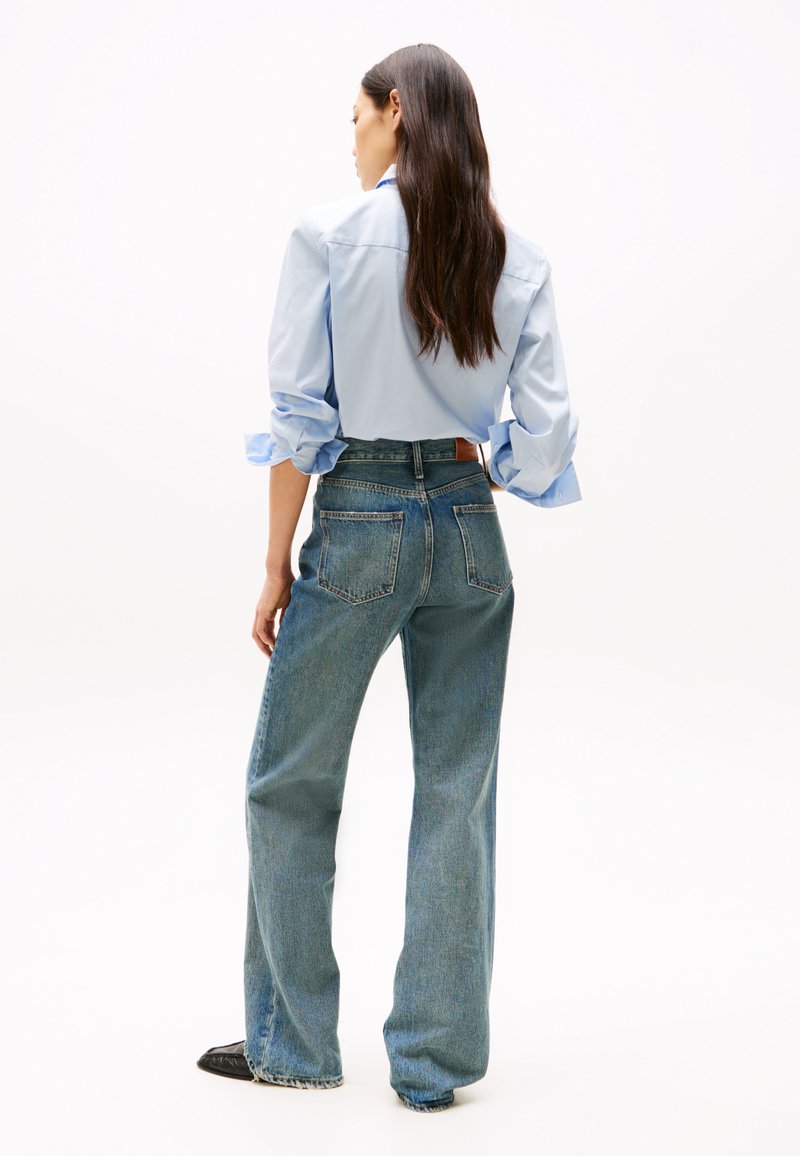 Lichtblauwe lange mouwen blouse met opgerolde manchetten, gecombineerd met hooggerimpelde lichtblauwe straight-leg jeans met opgestikte achterzakken.