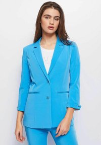 Lichtblauwe blazer met een getailleerde pasvorm, enkele knoopsluiting, reverskraag en twee voorzakken. Gladde textuur, op maat ontworpen.