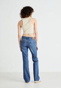 Light beige cropped tank top; blue straight-leg jeans with a brown Lee logo patch on the back waistband and two rear pockets.